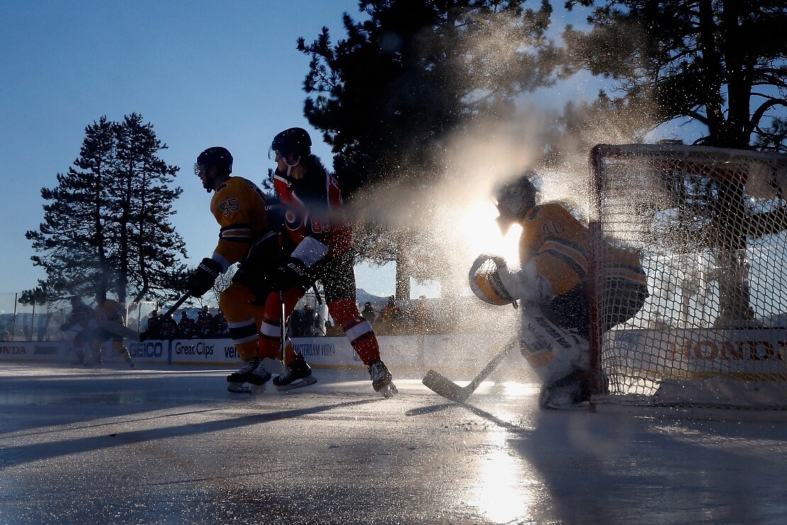 Zwei Eishockeyspieler vor einem Torwart, im Hintergrund Bäume