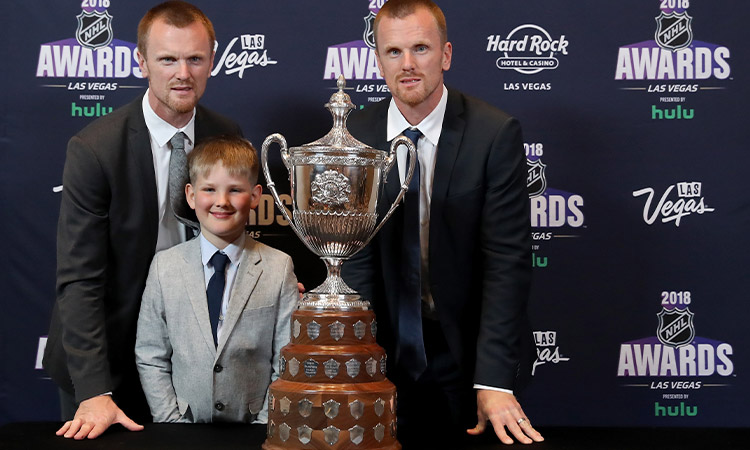 Die zwei Eishockeyspieler Henrik Sedin und Daniel Sedin stehen mit einem kleinem Jungen vor einem Pokal